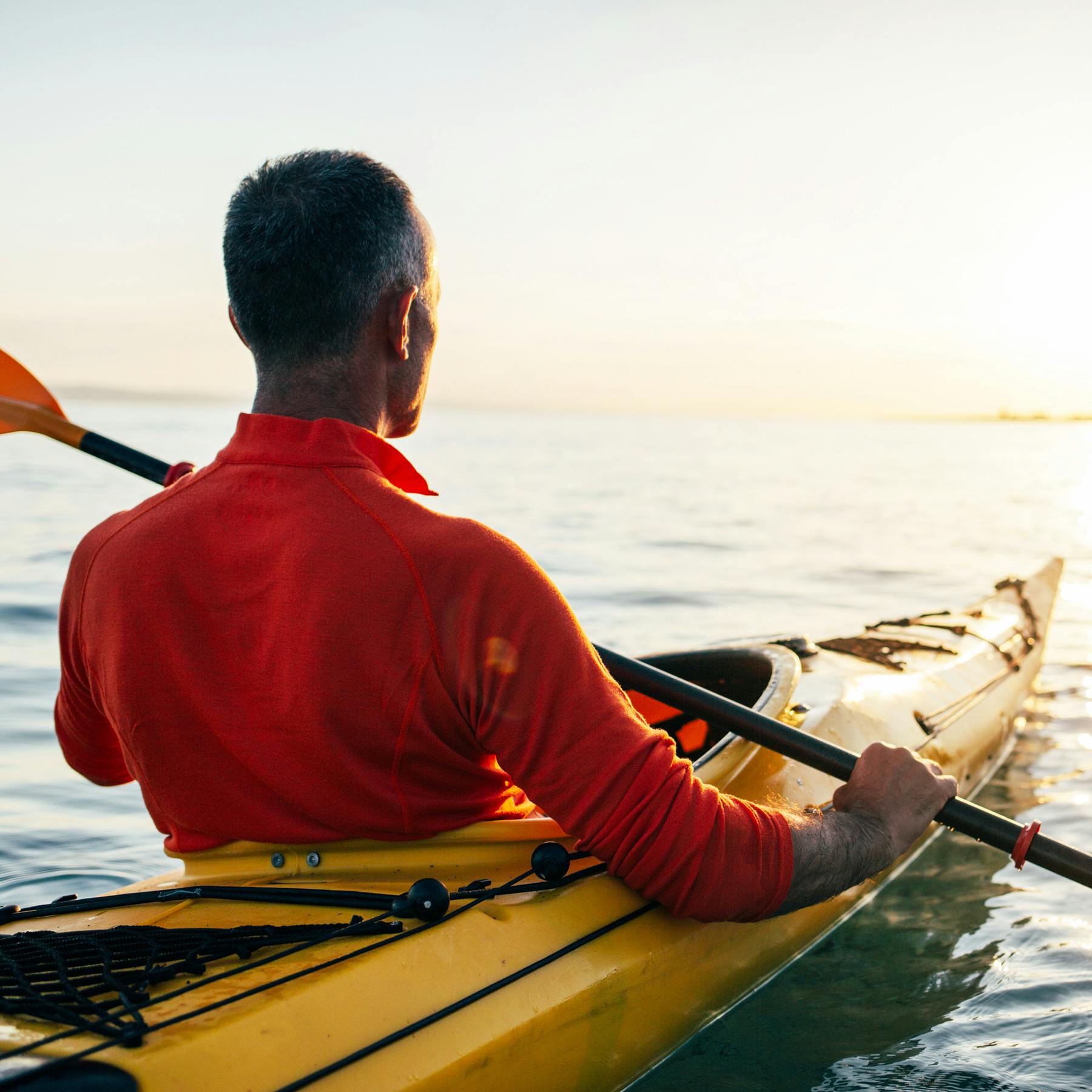 Man in kayak paddling in the ocean towards the sunrise.