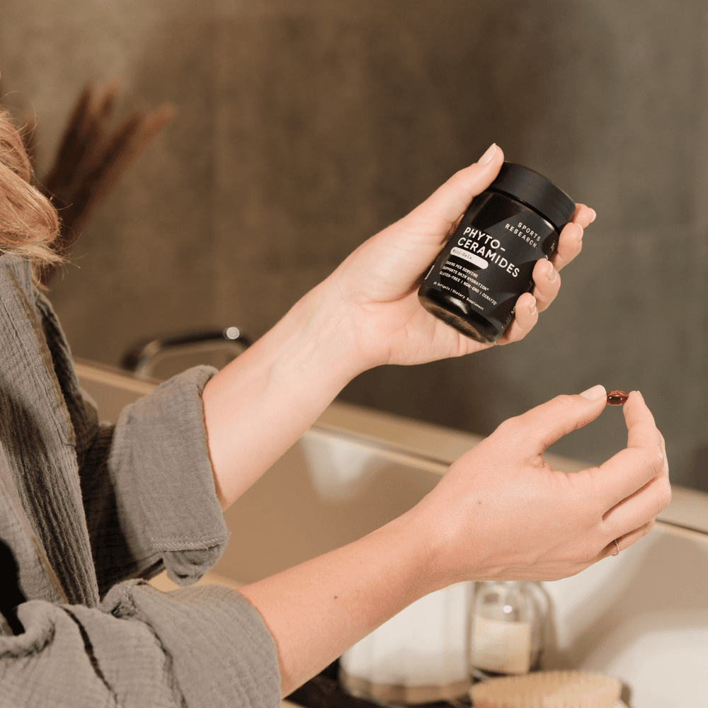 Lifestyle image of woman holding phytoceramides softgel and bottle.